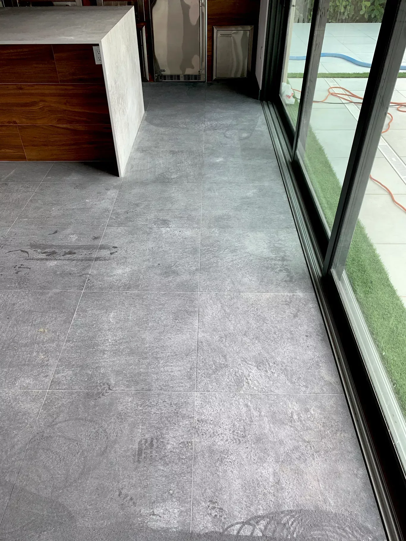 Empty gray-tiled hallway beside glass sliding doors, with a wood counter on the left.