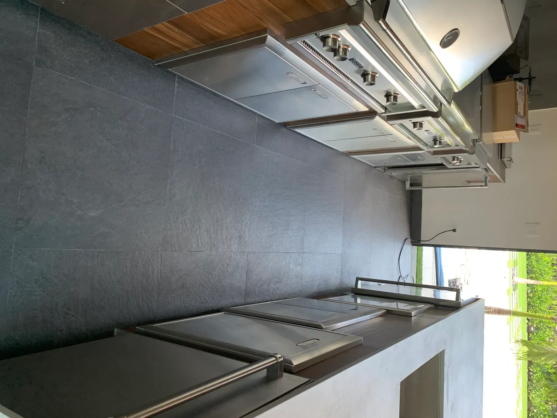 Modern kitchen with dark cabinets, stainless appliances, and a long gray floor with windows at one end