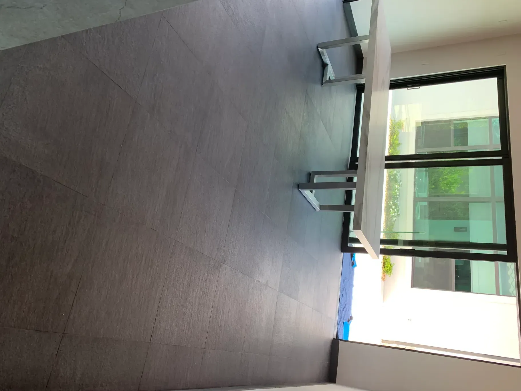Outdoor patio with dark wood flooring, glass doors, and a bright white wall with a blue tarp on the side
