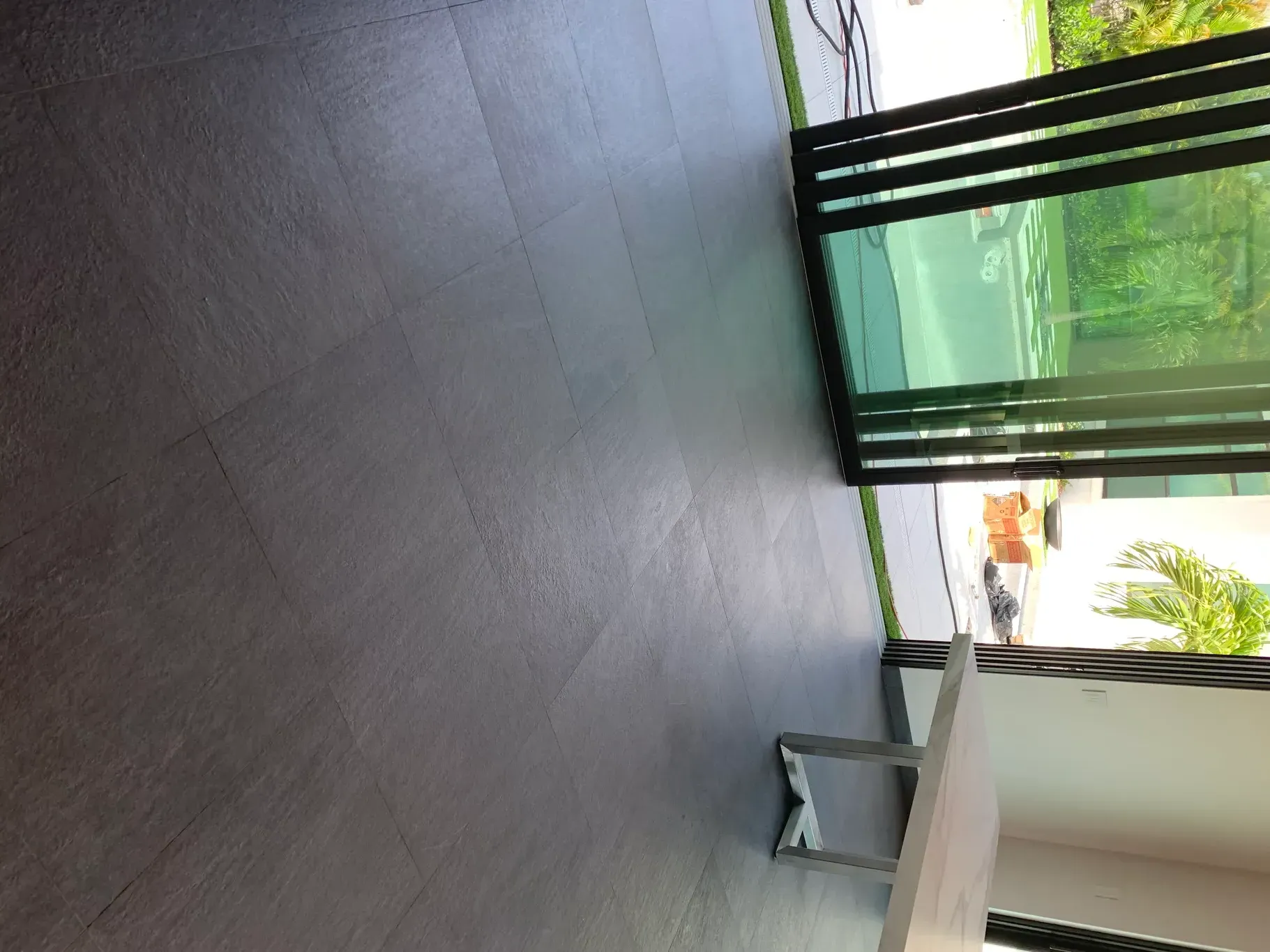 Covered patio with dark tile floor, a bench, and open doors to a green garden outside.