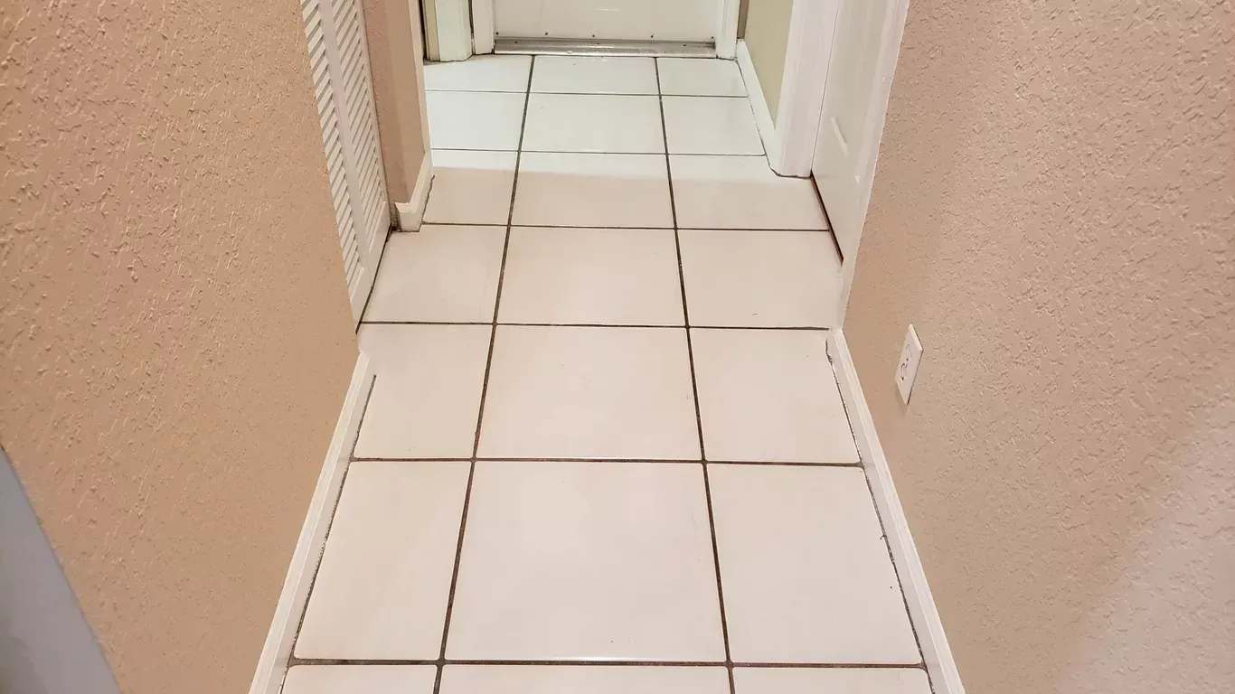 Narrow hallway with white tile floor and beige walls, leading to a closed white door.
