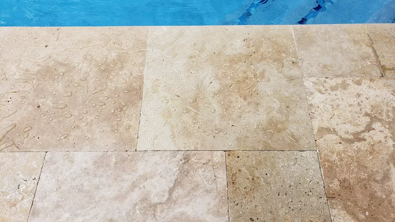 Beige stone tile surface beside a blue water edge