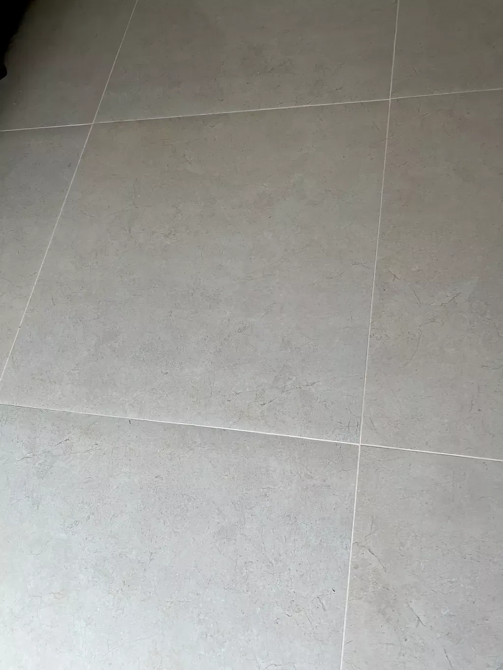 Close-up of light gray tiled floor with visible grout lines and slight surface wear