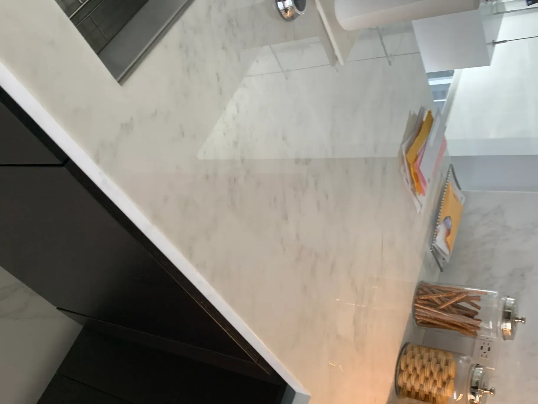 Modern kitchen countertop with bowls of wooden utensils and packaged items on a marble island
