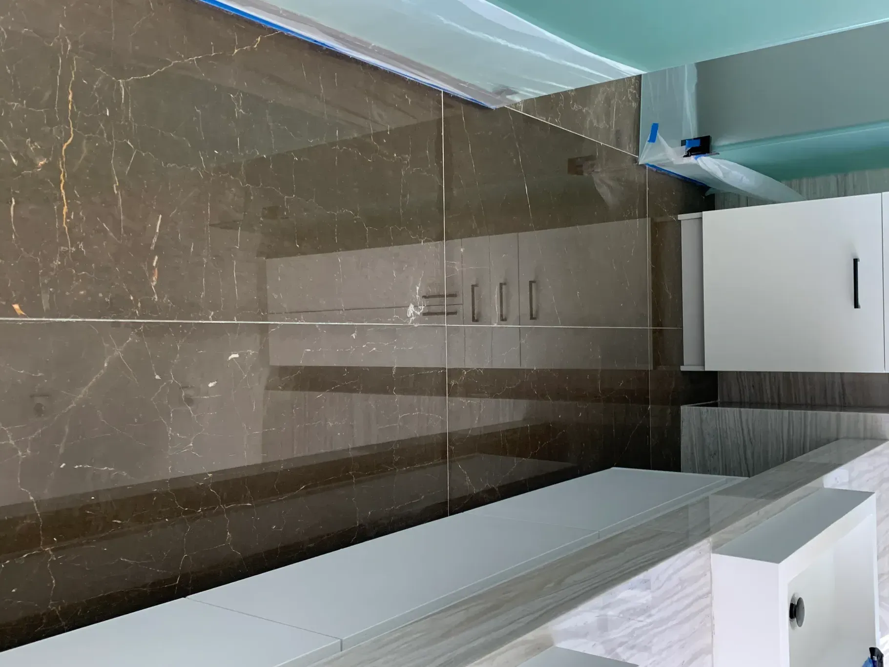 Modern kitchen with glossy dark tile floor, white cabinets, and a stainless-steel refrigerator