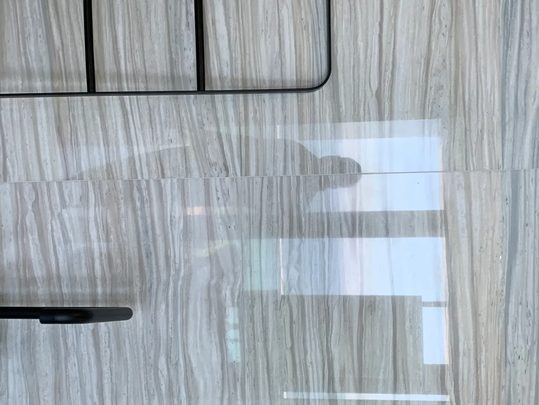 Wood-grain cabinet door with black handles and a bright window reflection