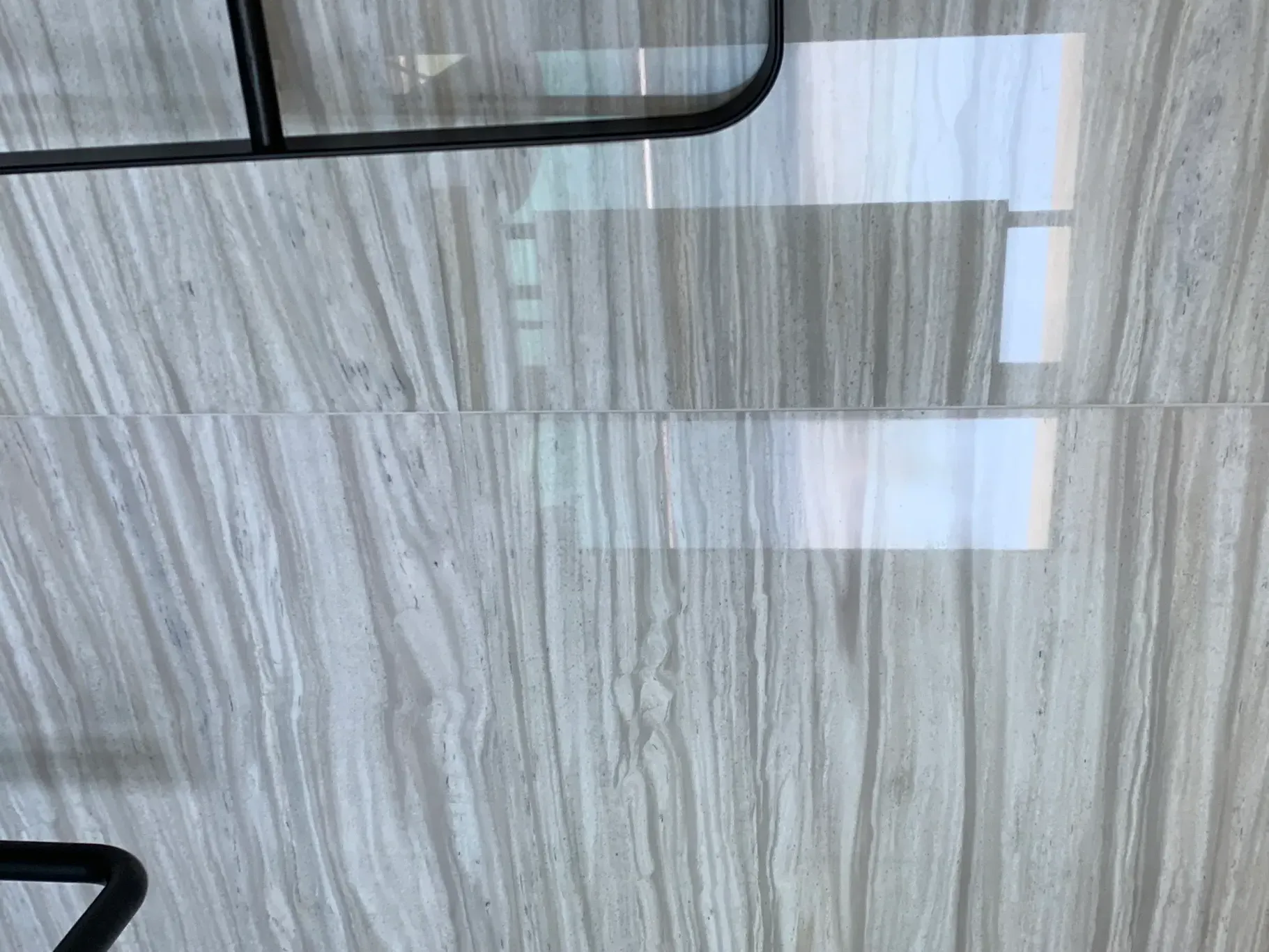 Gray marble-tile wall with a black-framed glass panel and white rectangular reflections