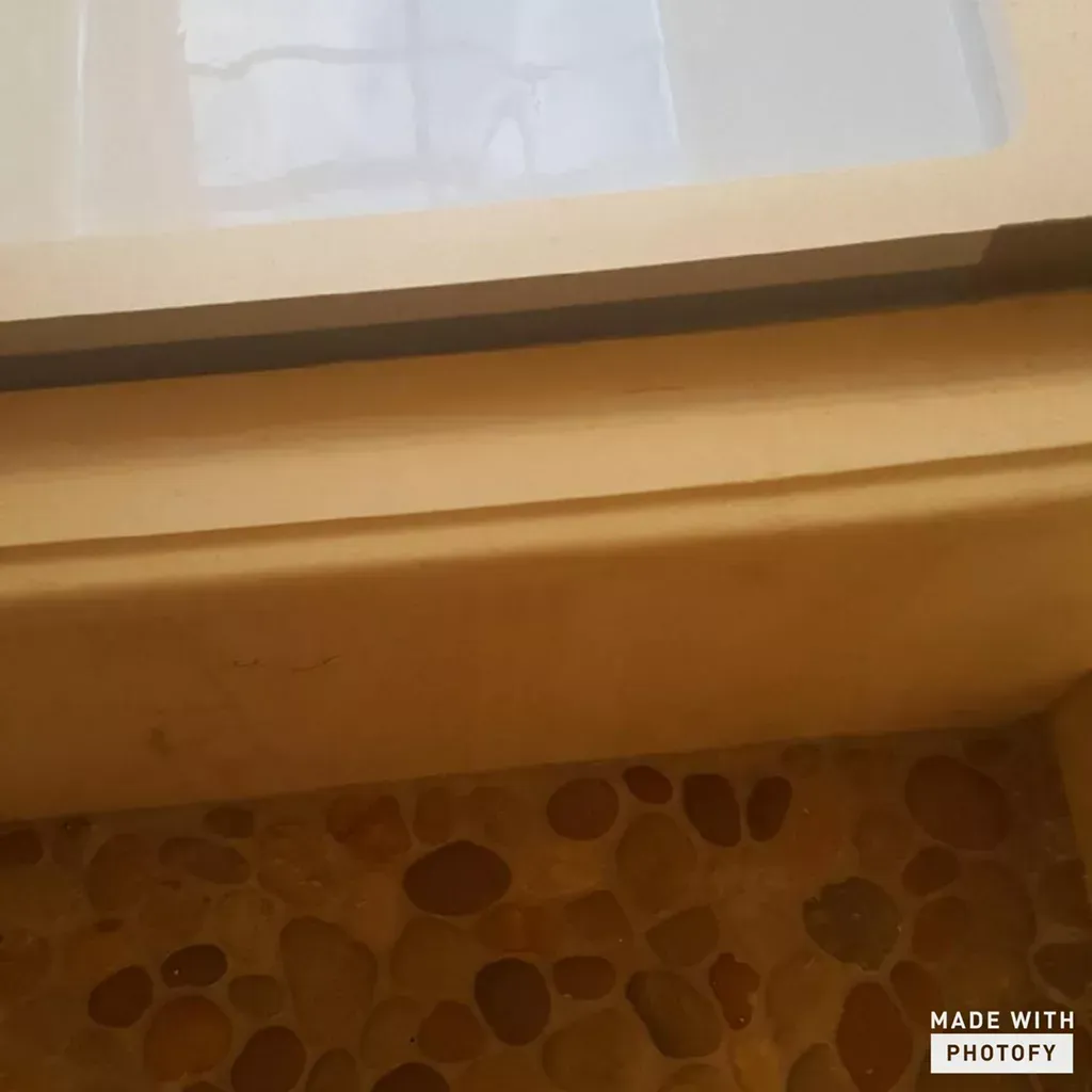 Wooden windowsill above a pebble-pattern floor, with a small white sign or sheet at the top.
