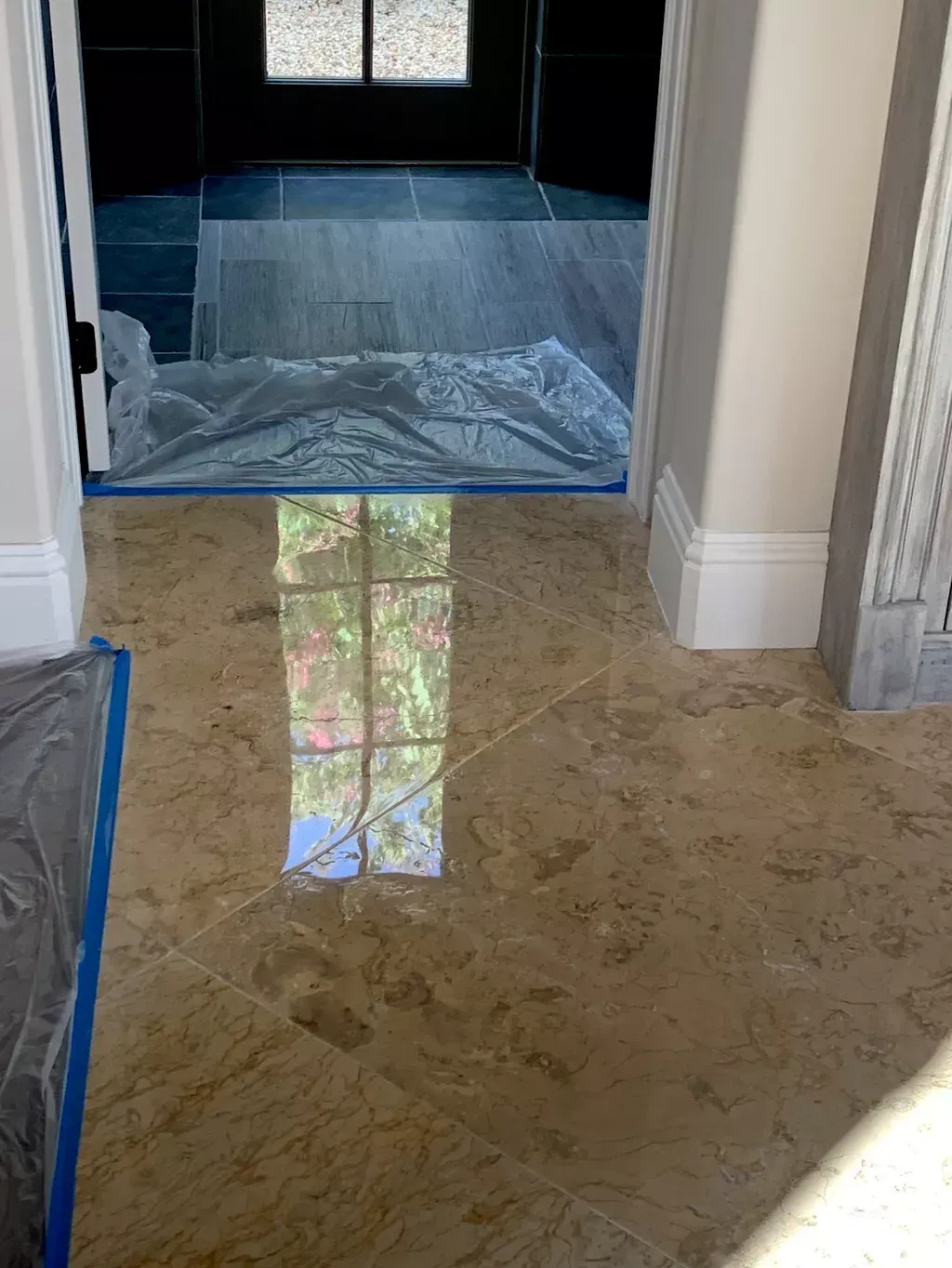 Tiled hallway with blue painter’s tape and plastic sheeting covering the floor near a doorway