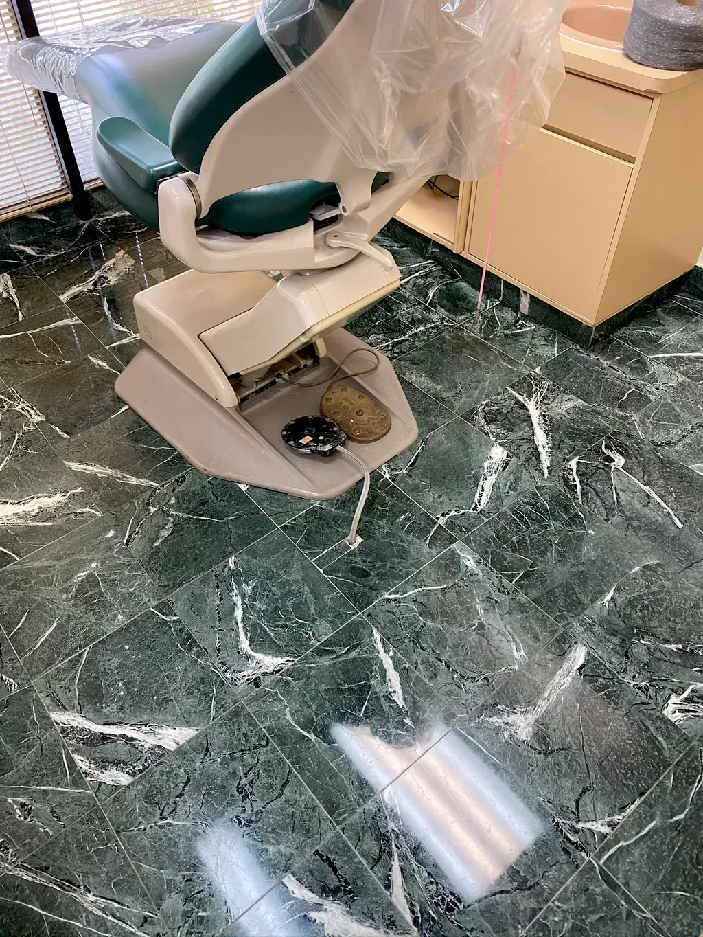 Dental chair covered in protective plastic in a clinic with green marble tile floor