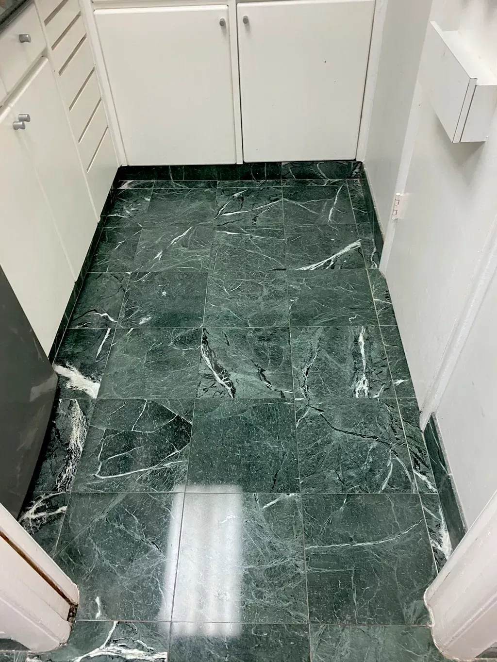 Narrow kitchen aisle with dark green marble floor and white cabinets on both sides.