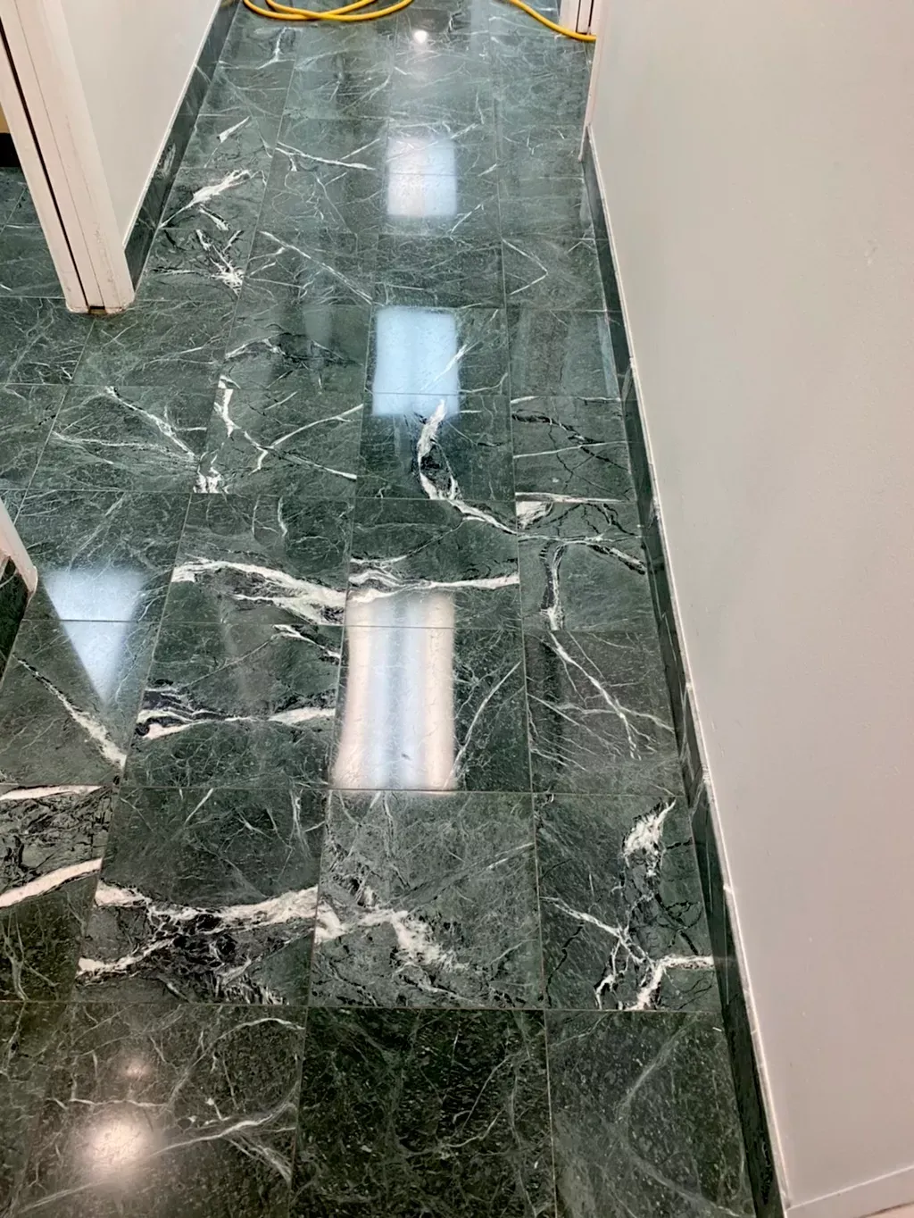 Shiny green marble floor in a narrow hallway with white walls and reflections of overhead lights