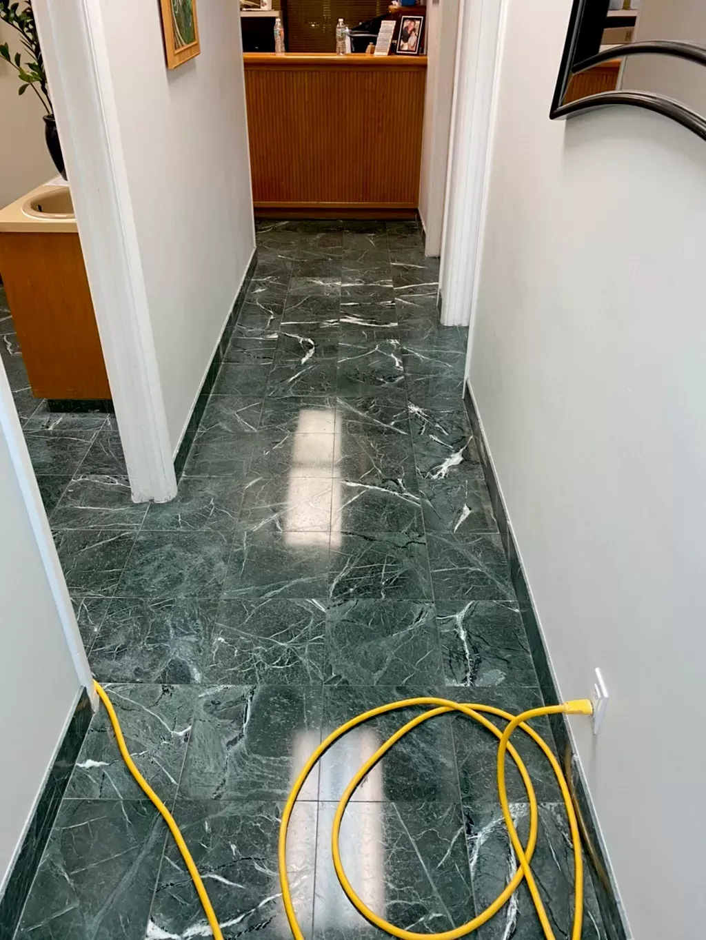 Narrow hallway with green marble floor and yellow cable coiled on the floor near a doorway.