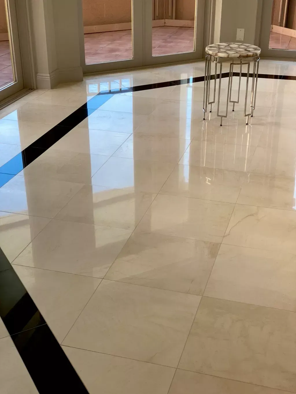 Glossy marble lobby floor with black inlay, glass doors, and a small round side table