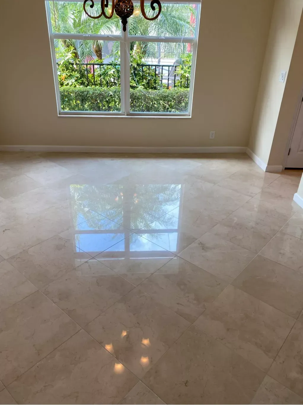 Empty room with glossy marble floor, large window, and chandelier reflections