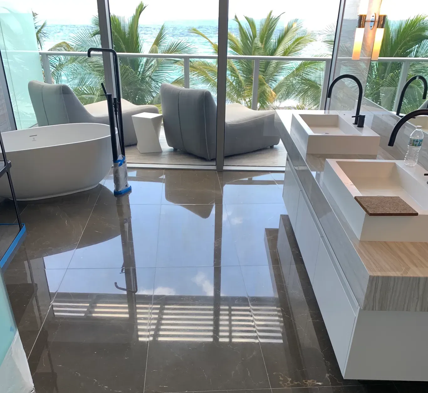 Modern living room with glossy tile floor, large windows, gray chairs, white sink island, and ocean view.
