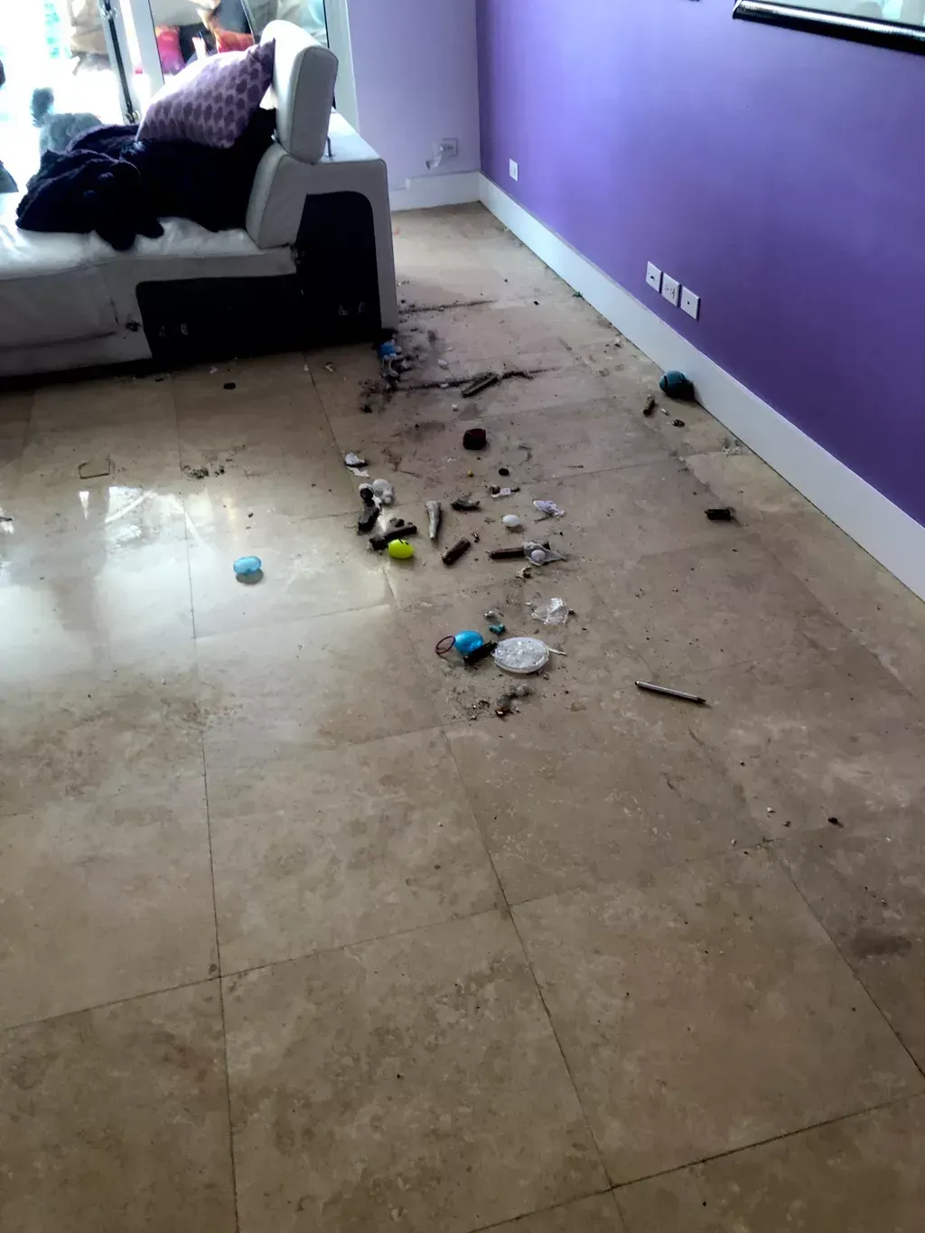 Living room floor with scattered trash and debris beside a sofa and purple wall