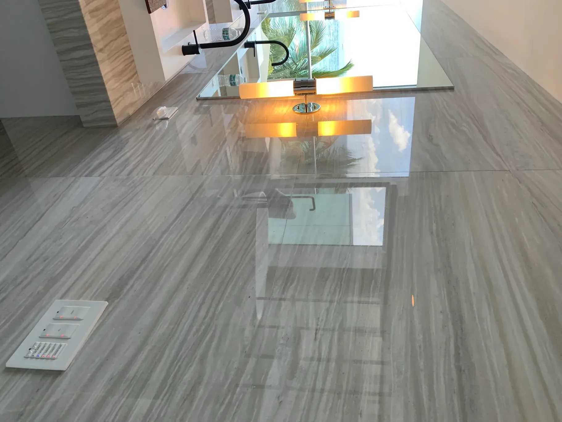 Modern tiled lobby with glossy floor, glass table, and warm orange lights reflected on the surface.