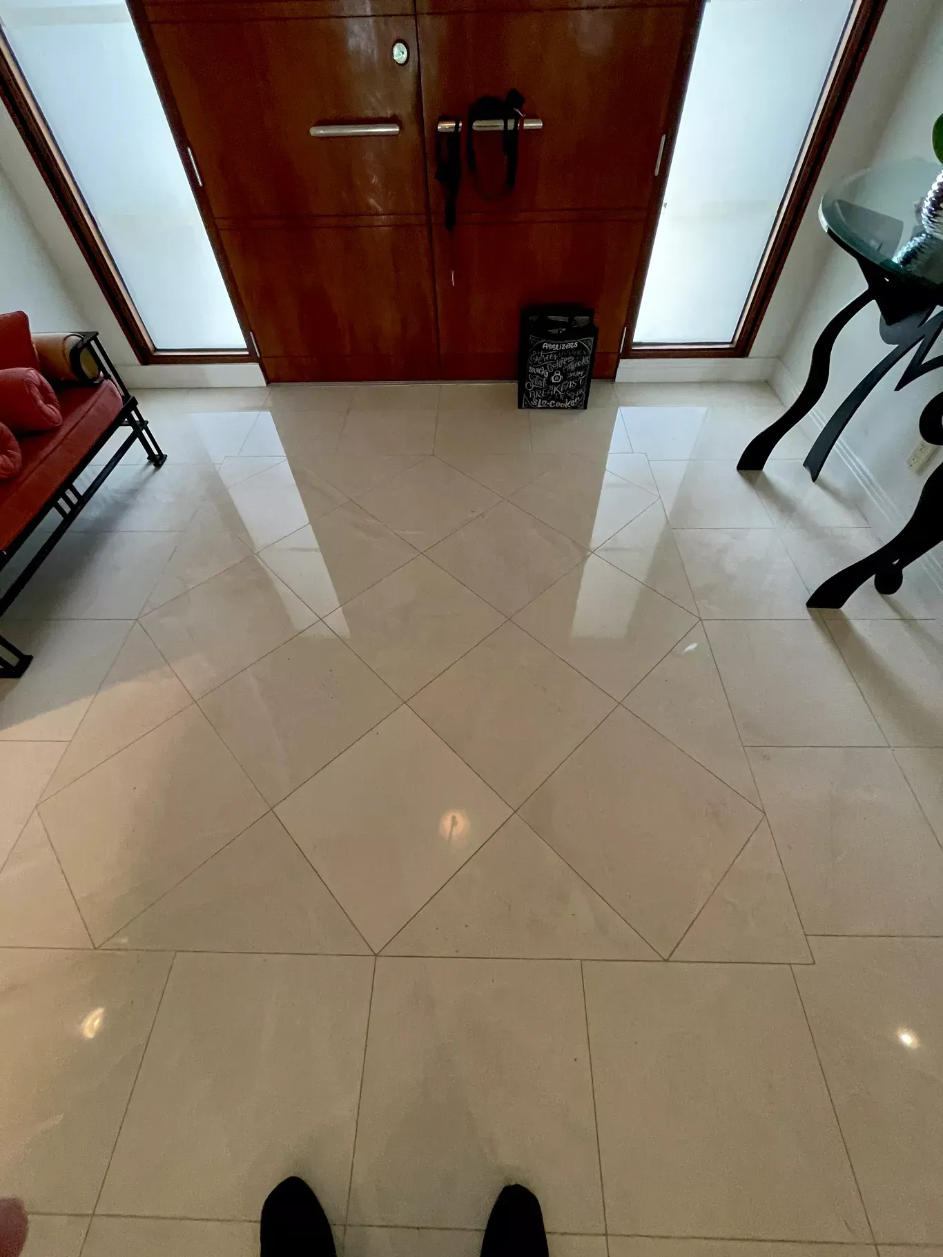 Indoor hallway with beige tiled floor, wooden double doors, and a black chair on the right.