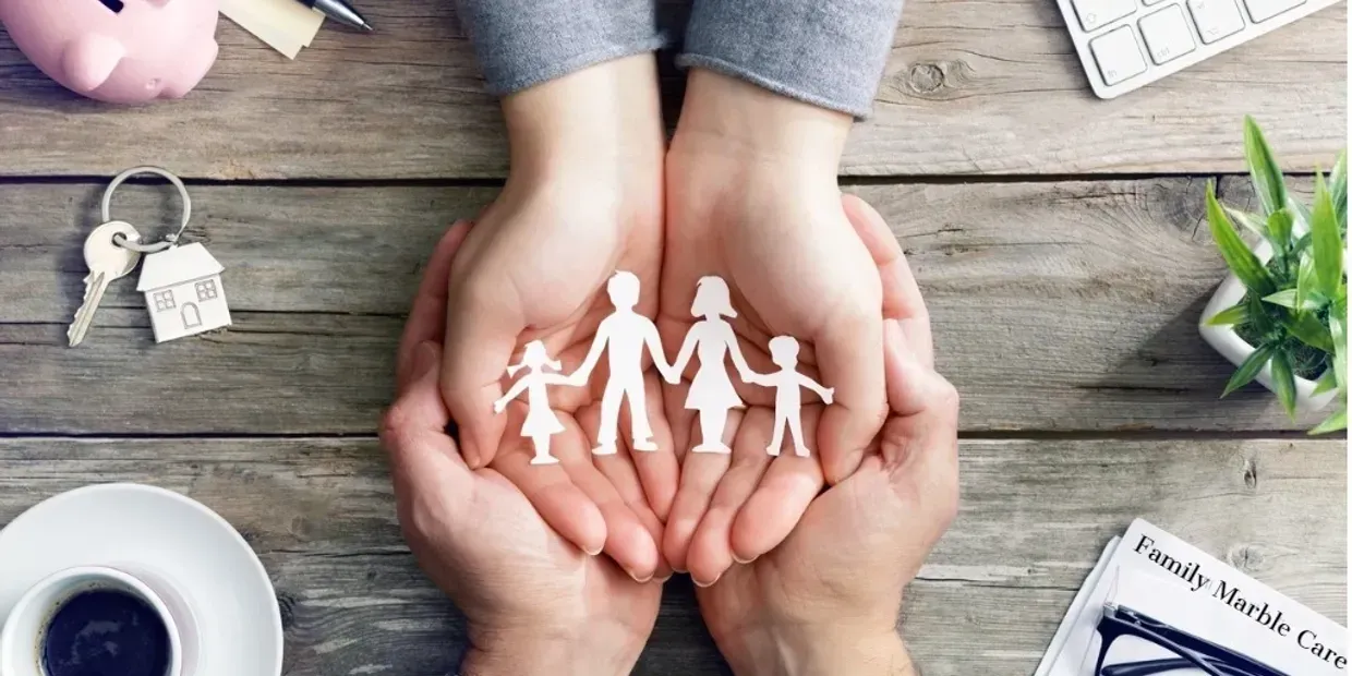 Hands holding paper cutout family figures on a wooden table with notebook and coffee cup