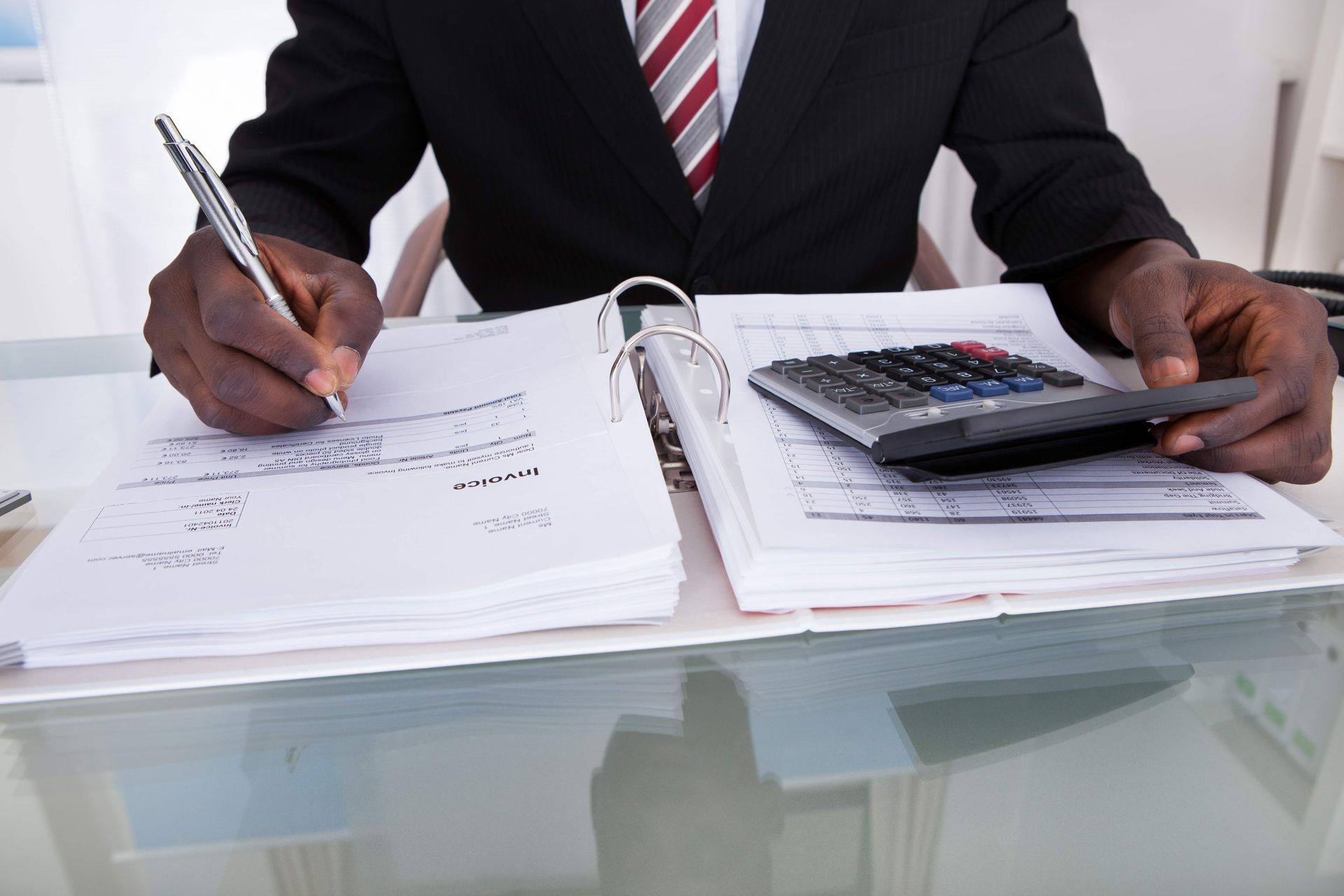 A man in a suit and tie is using a calculator and writing in a binder.