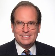 A man wearing glasses and a suit and tie is smiling.