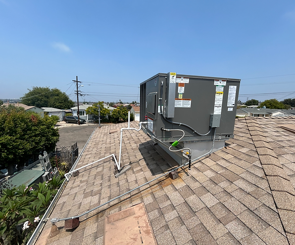 A large gray HVAC unit installed on a residential shingled roof under a clear blue sky.