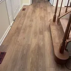 Wooden floor hallway next to a staircase with wood banister and white door.