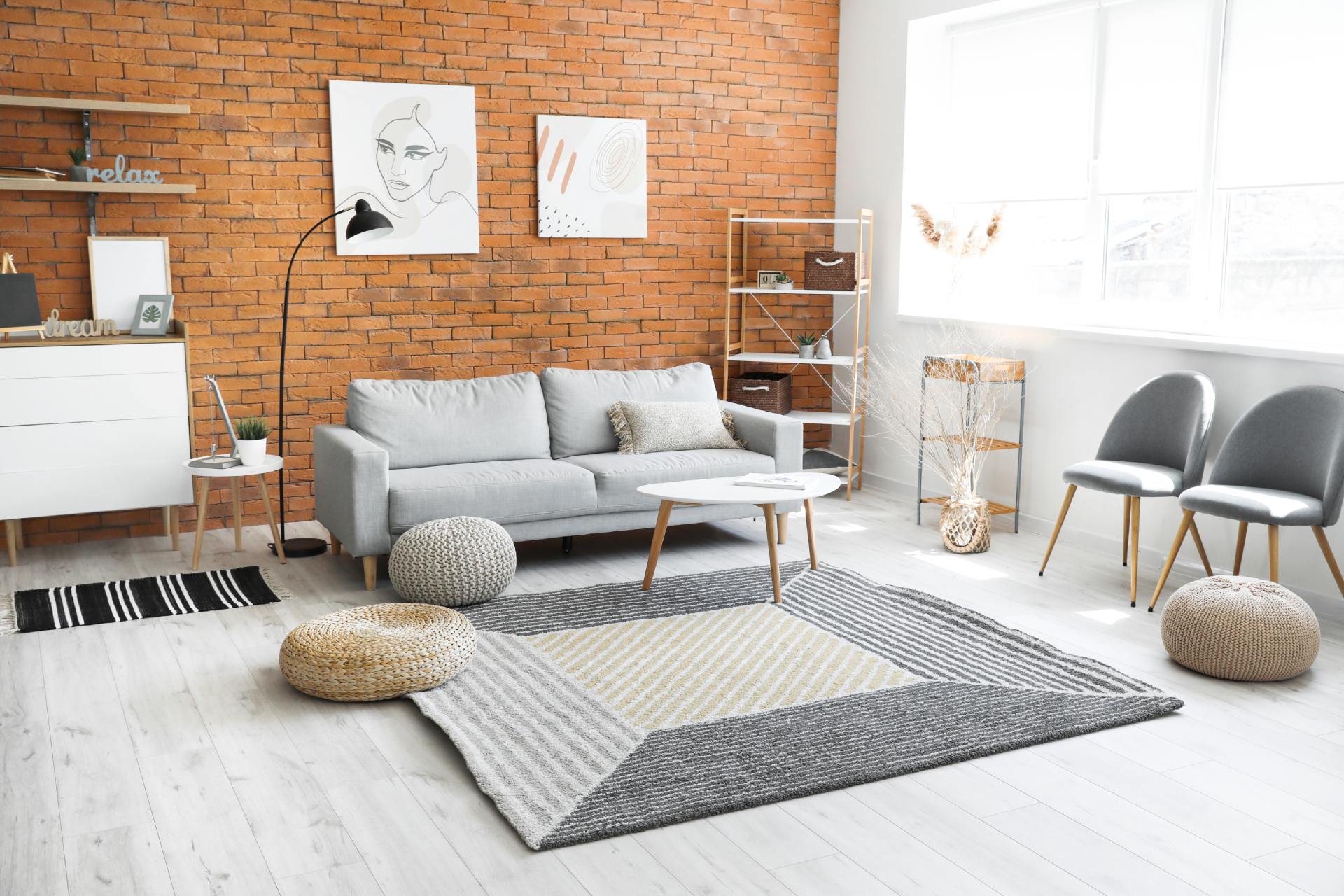 Living room with brick wall, gray sofa, area rug, small tables, and artwork.