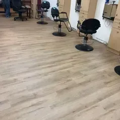 Salon interior with several black styling chairs on light wood-look flooring.