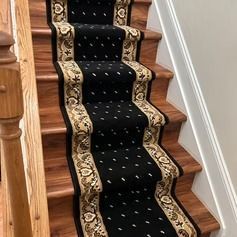 Staircase with black carpet runner featuring floral design and beige borders; wood steps visible.