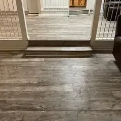Gray wood-look flooring with a short set of steps leading to a slightly elevated area, white railings visible.