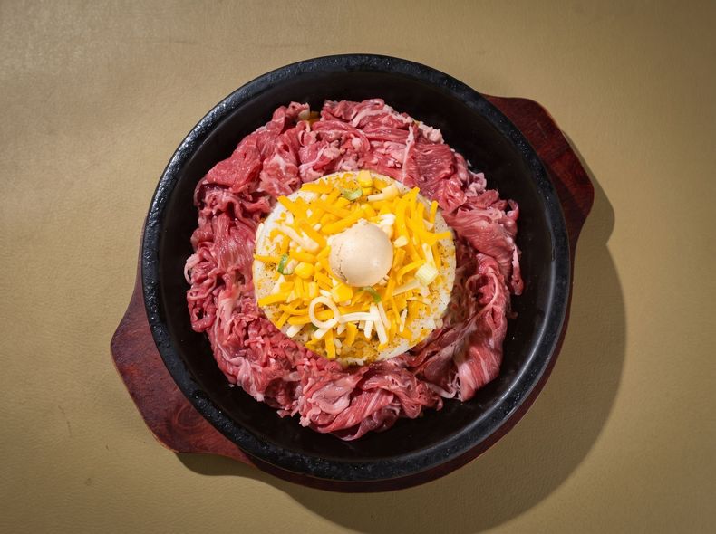 Raw beef arranged in a ring around a bowl of noodles topped with a yolk on a tan background