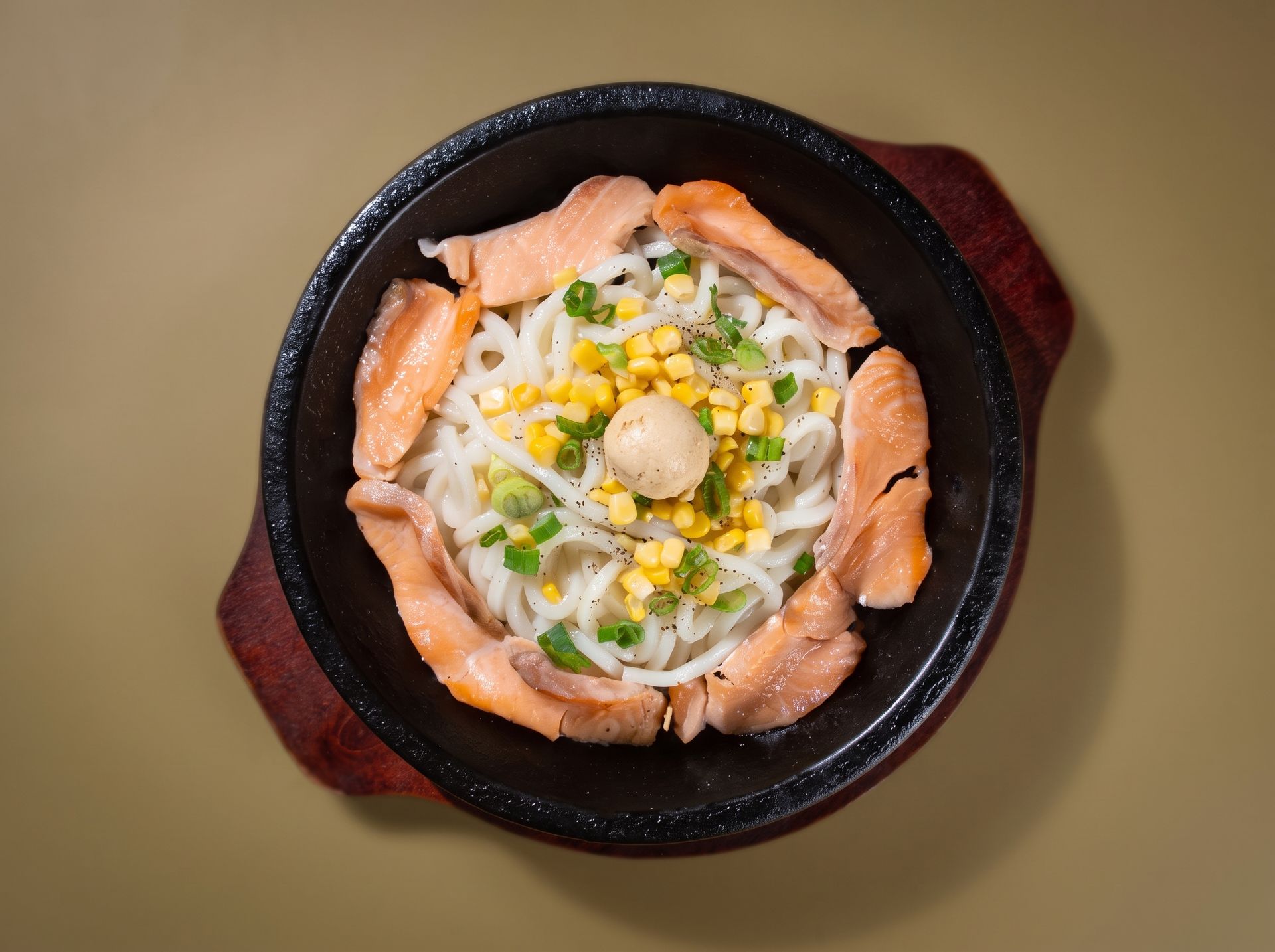 Salmon sashimi arranged around a rice bowl topped with corn and green onion in a black bowl