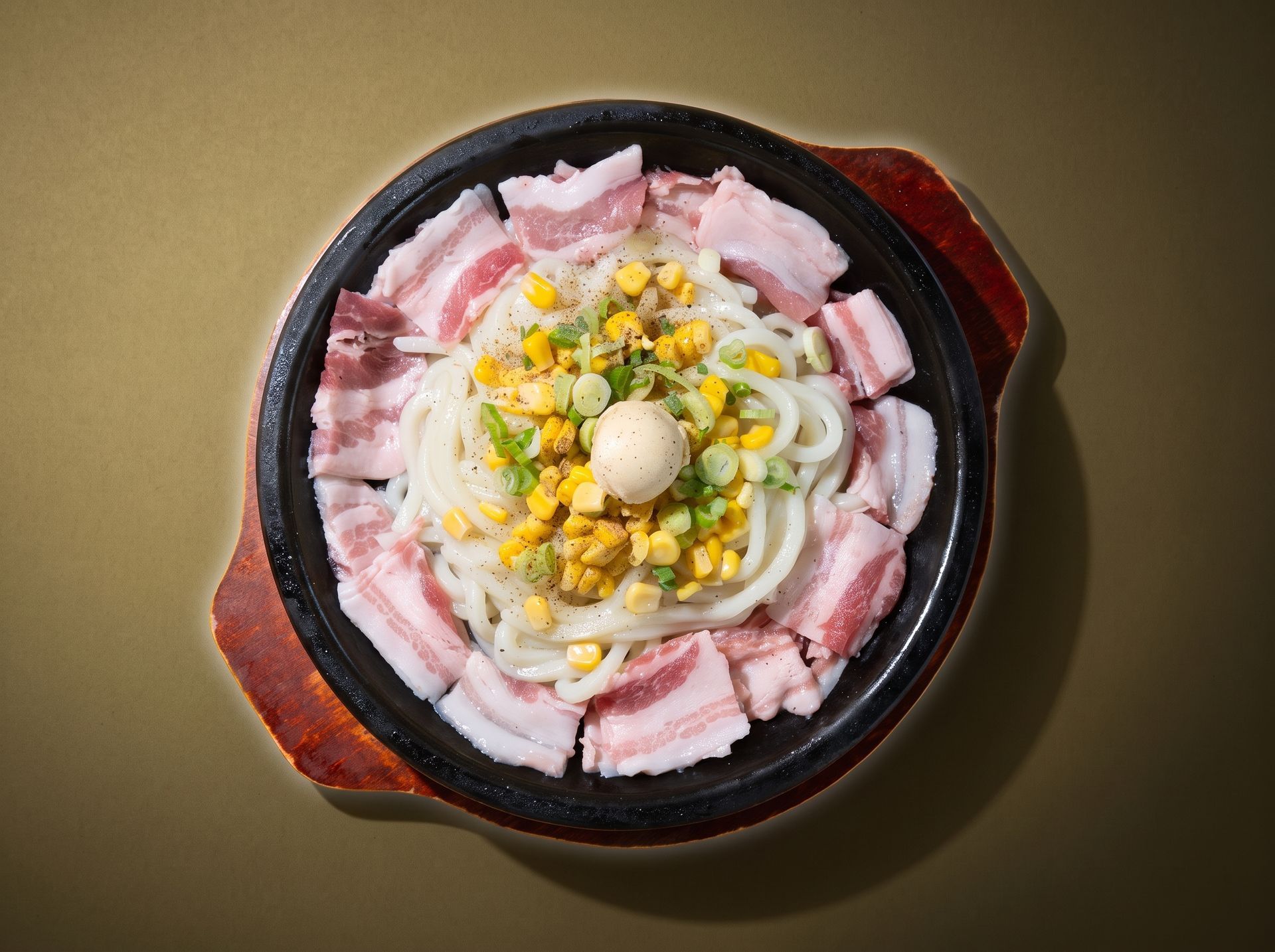 Top-down view of a bowl of sliced pork, corn, and noodles on a dark table