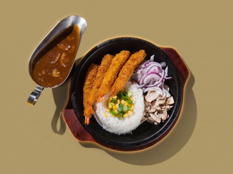 Curry cutlet rice with sliced onions and cabbage in a black bowl, with a side of brown sauce in a ladle