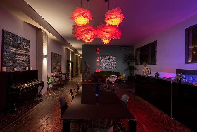 Un interno elegante e dalle luci soffuse, con lampade a sospensione rosse, un tavolo da pranzo scuro, un pianoforte e un'accogliente zona salotto.