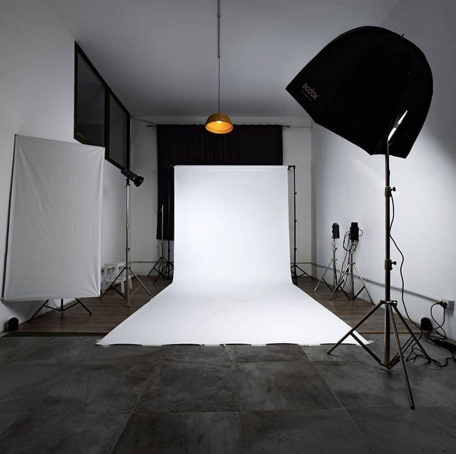 Uno studio fotografico con sfondo bianco, attrezzatura di illuminazione softbox, un riflettore e una lampada a sospensione.