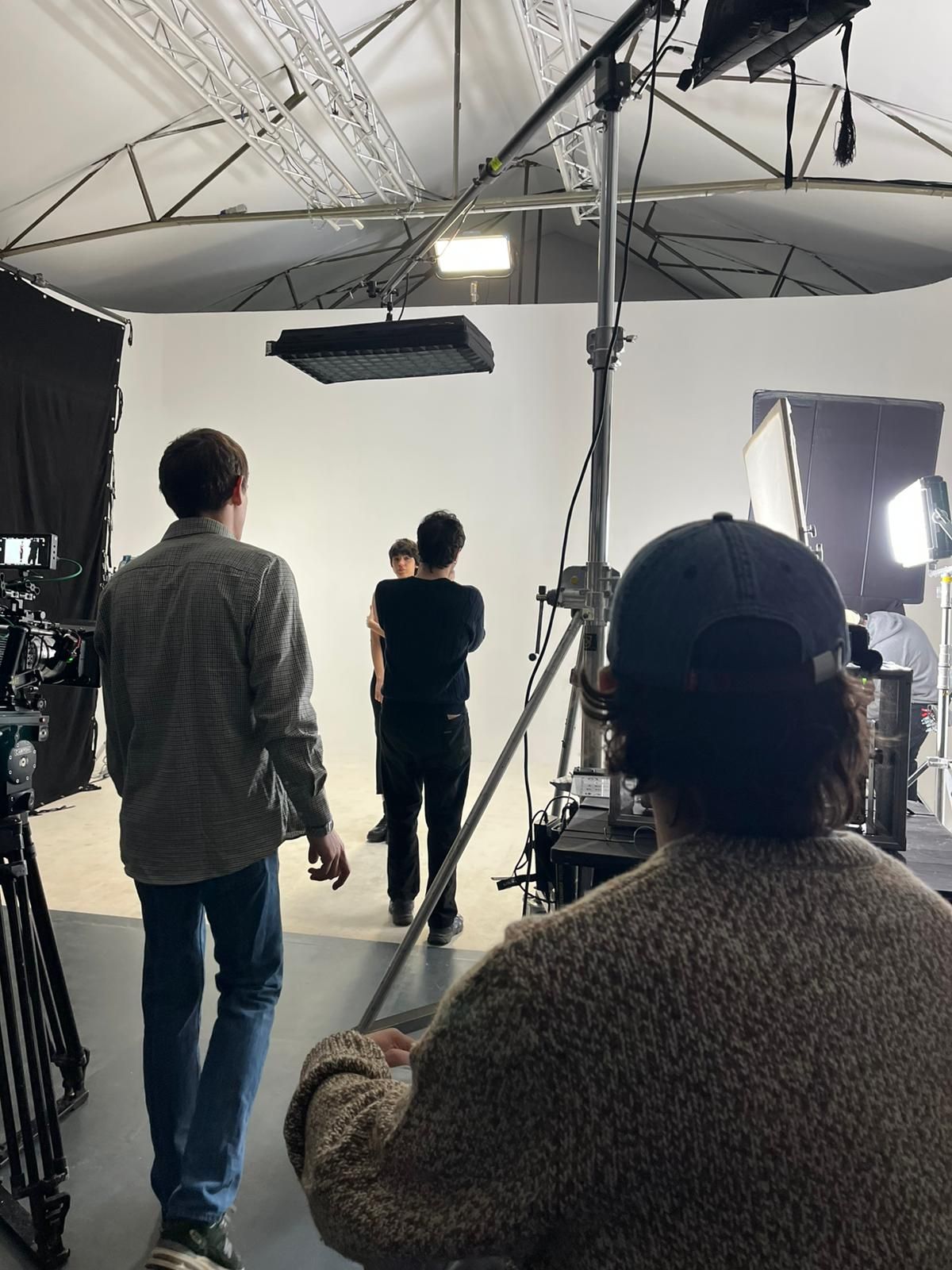 Una troupe cinematografica riprende un gruppo di persone sedute insieme su un grande divano in un salotto interno illuminato a giorno.