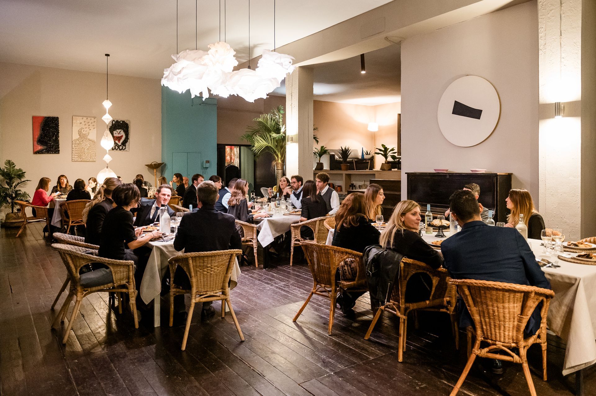 Un gruppo di persone cena a un tavolo in un lussureggiante patio all'aperto, illuminato di notte da calde luci sospese.