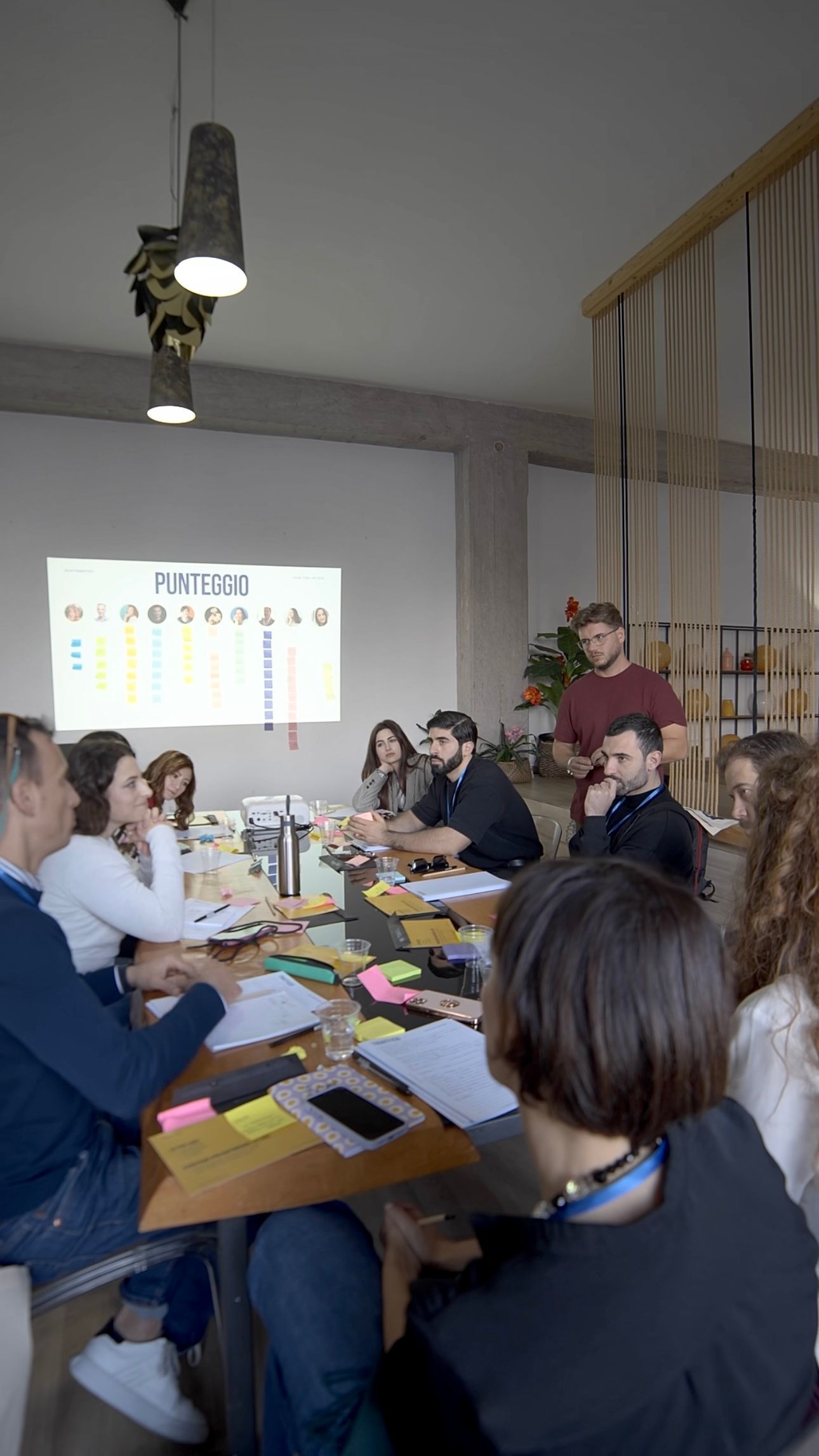 File di sedie di plastica trasparente disposte in una stanza ben illuminata con ampie finestre, tende leggere e pavimento in legno.