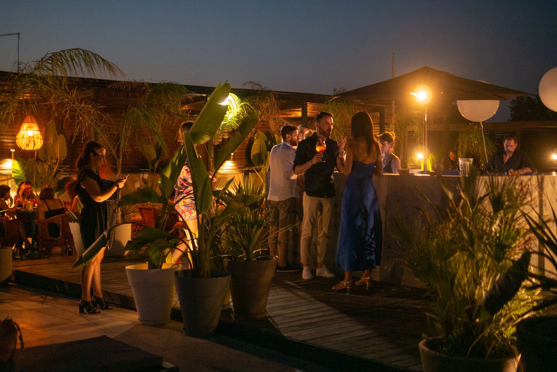 Una terrazza a bordo piscina con diverse zone salotto arredate con mobili in vimini, un divano verde e piante di agave in vaso.
