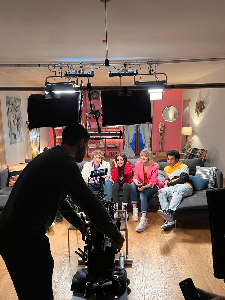 Una troupe cinematografica si prepara per le riprese in studio, con due persone in piedi davanti a uno sfondo bianco sotto luci professionali.