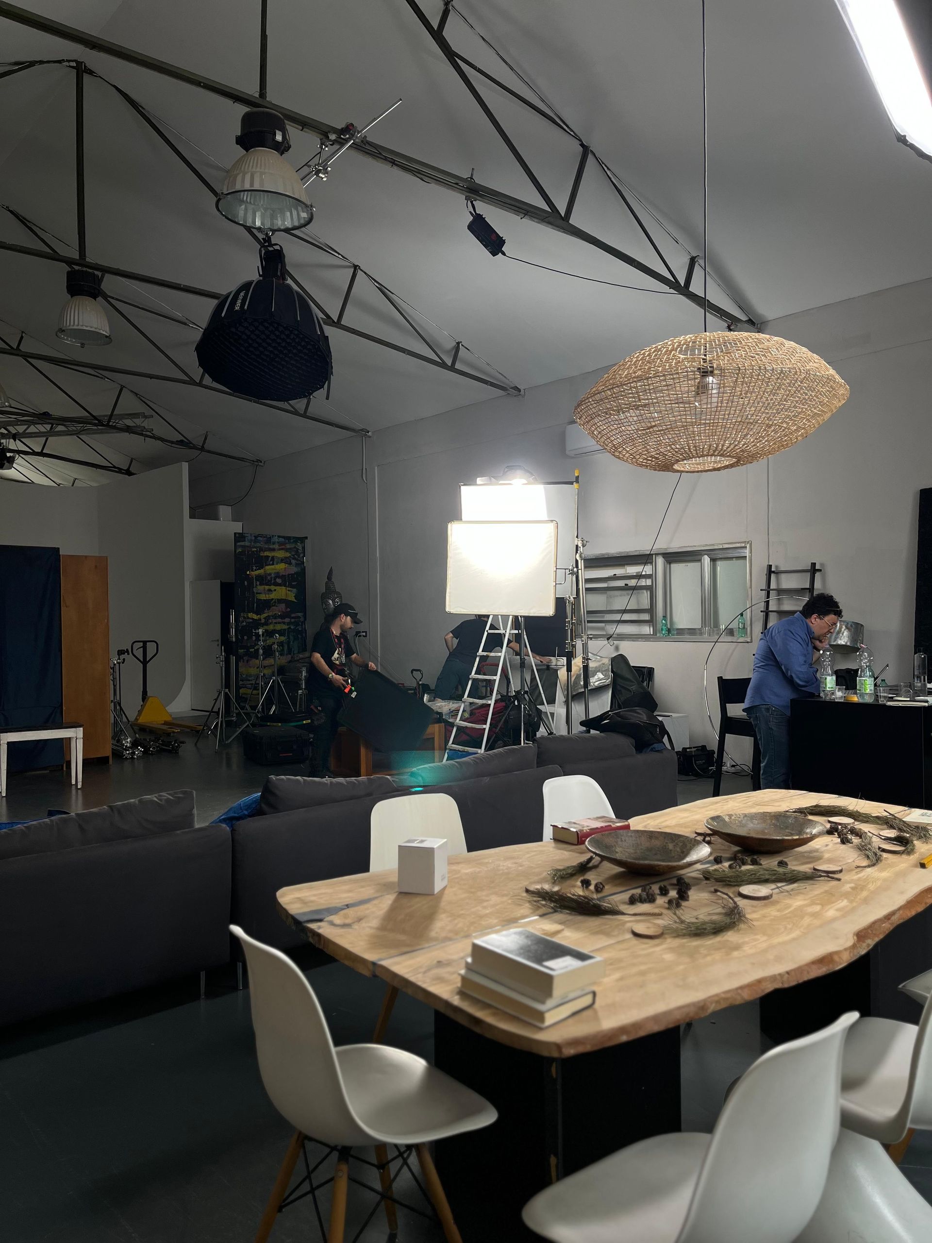 Un operatore di ripresa filma sei persone sedute su un divano in un salotto allestito come studio, con illuminazione professionale dall'alto.