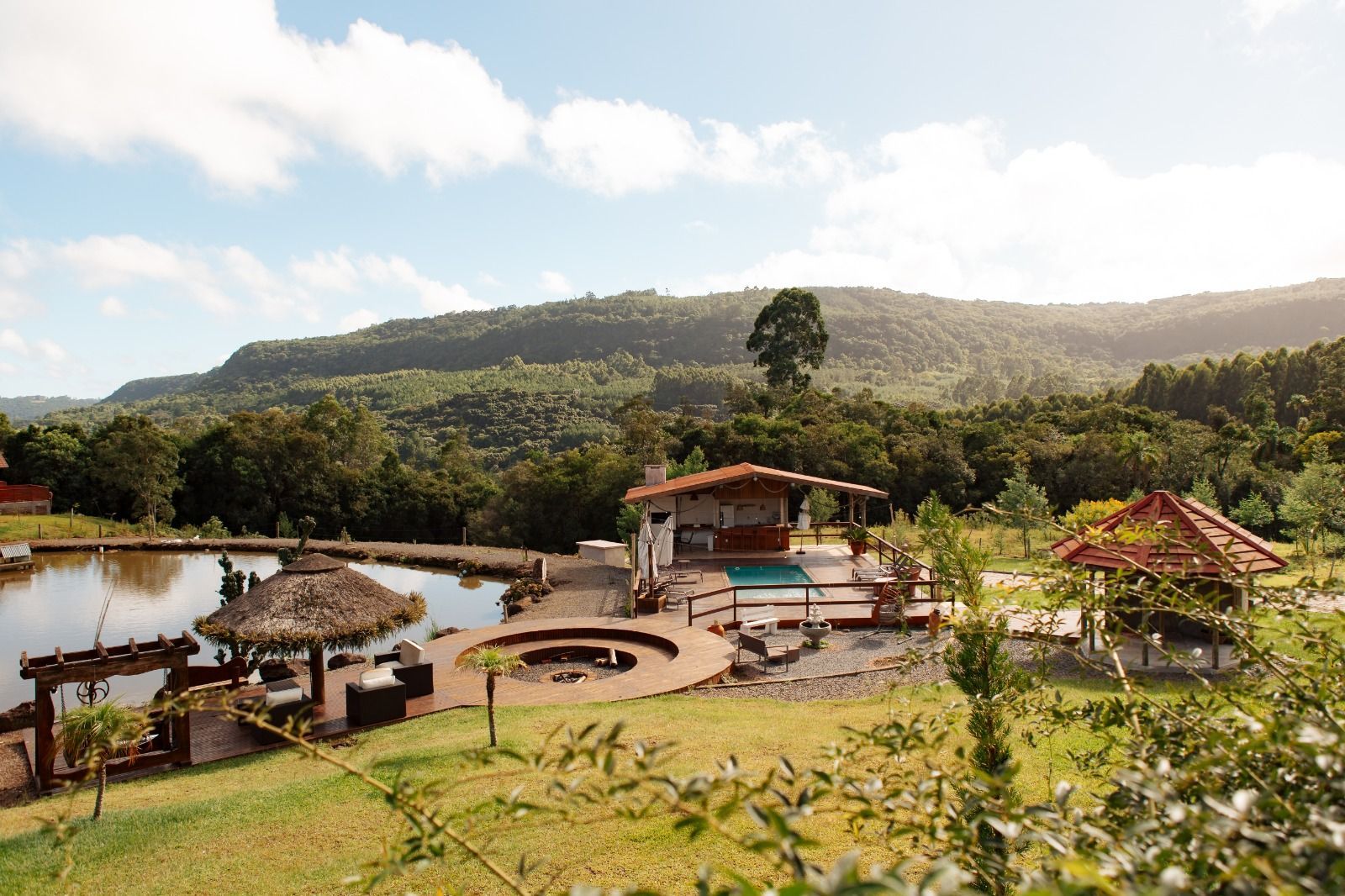 Resort à beira do lago com cabanas de palha, piscina e uma colina verdejante sob um céu estrelado.