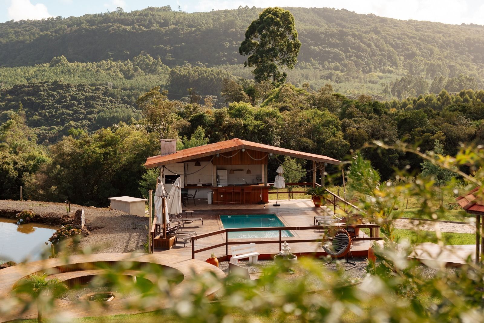 Cabana tropical na encosta de uma colina com piscina turquesa, rodeada por uma exuberante floresta verde.