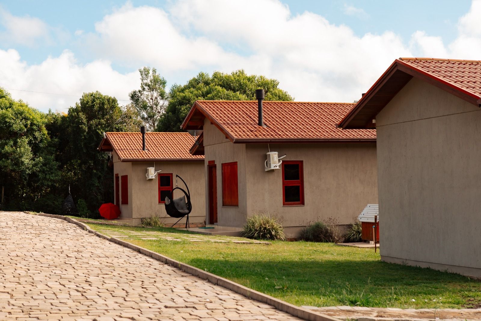 Casas com telhados vermelhos ao lado de uma rua de paralelepípedos com gramado verde e árvores sob um céu claro.
