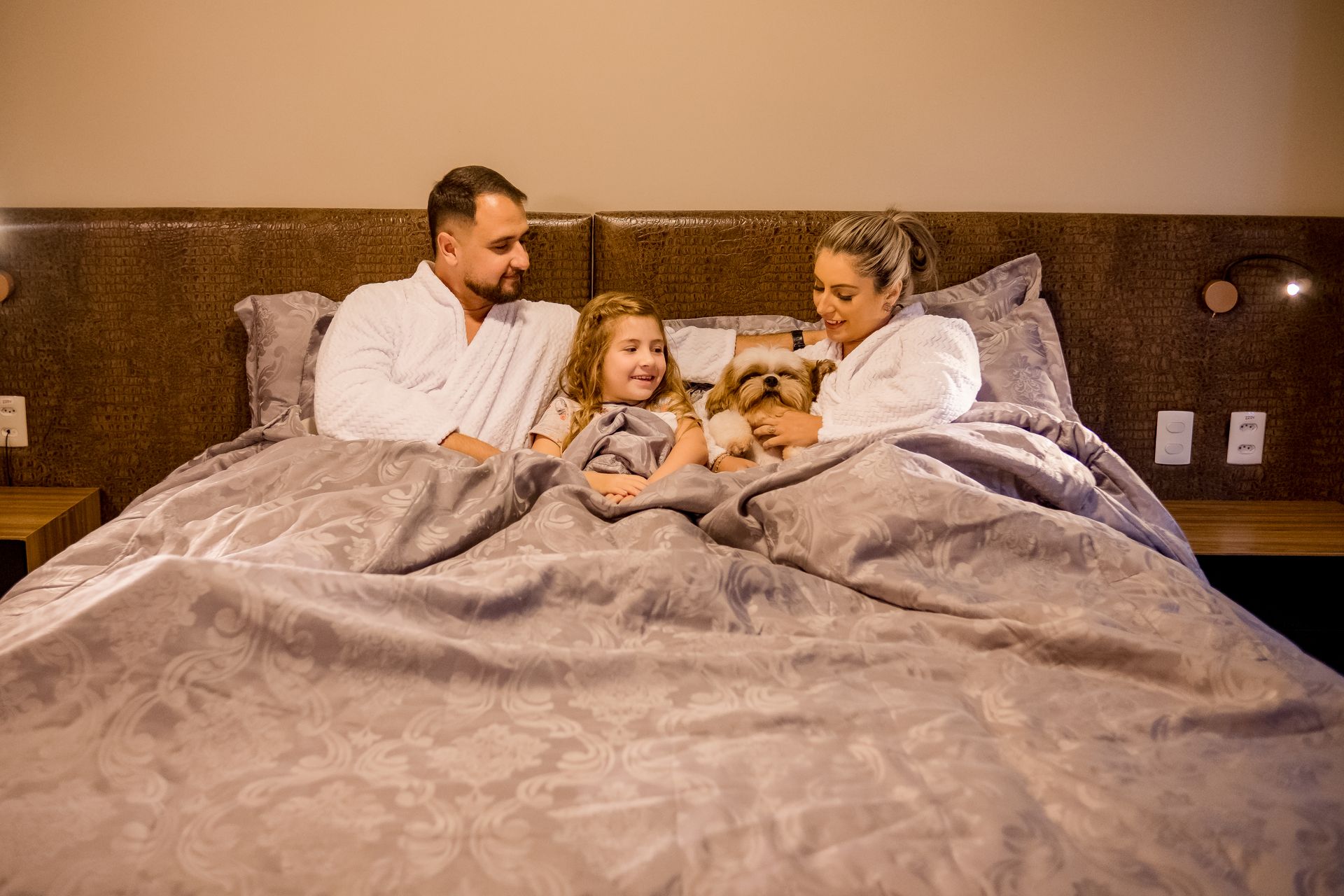 Uma família está deitada na cama com um cachorro.