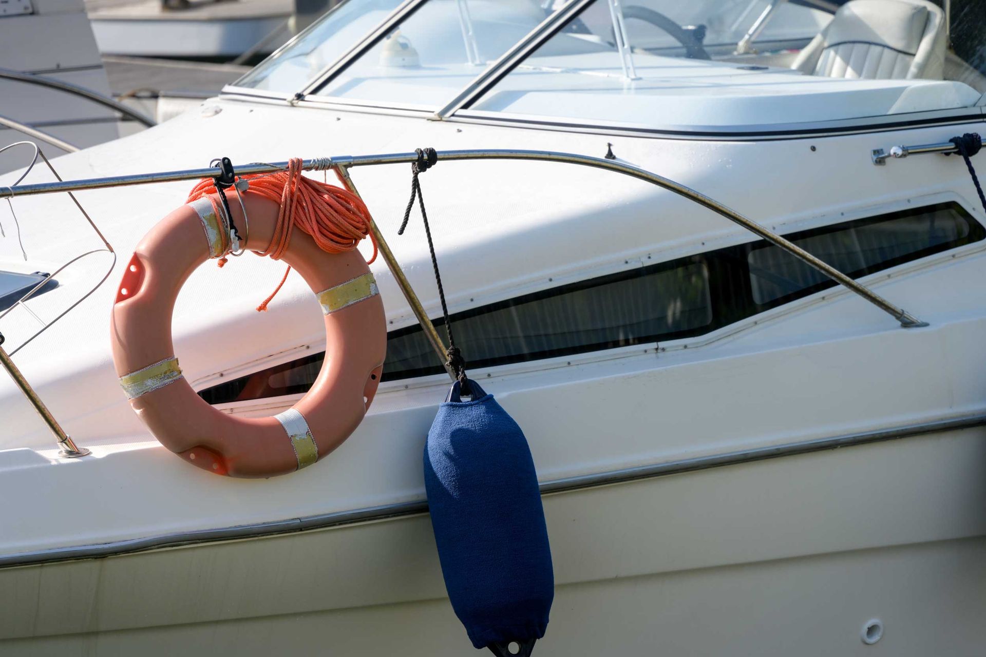 A white boat's side showing a mounted lifebuoy with attached rope and a fender hanging.