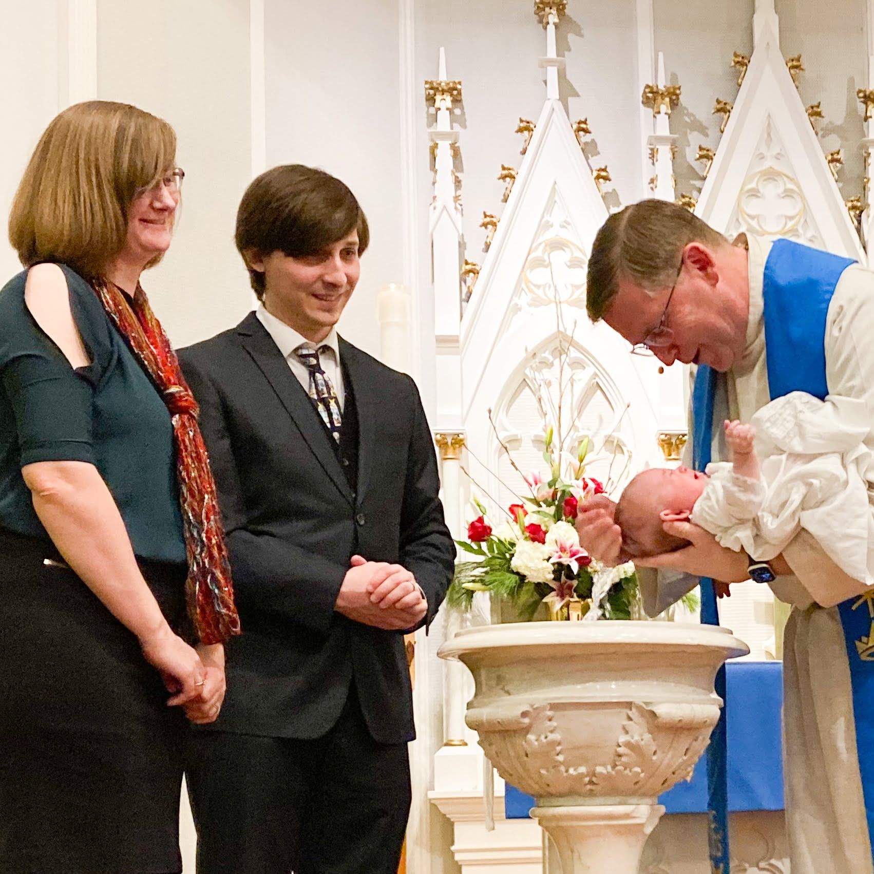 Two people watch as a pastor baptizes an infant